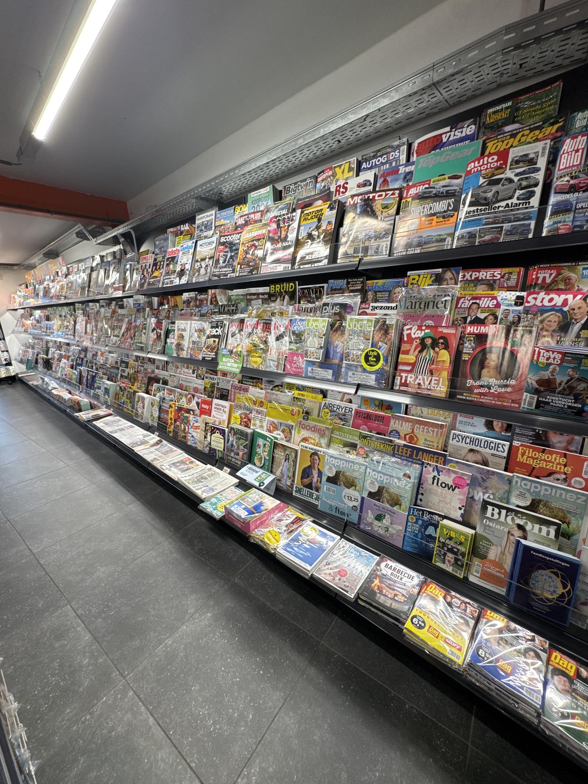 De perswand van LUX 2.0 over de volle lengte, met tijdschriften in de verlichte schappen en de kranten onderaan